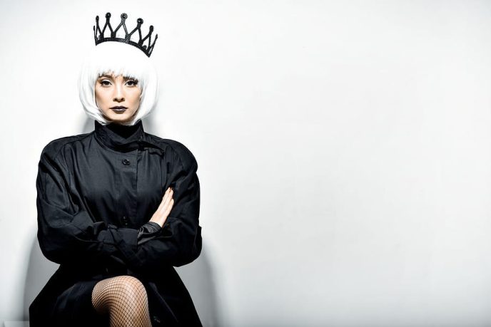 Black queen. A stern look. Black crown. A princess. Maleficent. Girl with a black crown decorated with precious stones sitting in studio on light background. Dark lipstick.